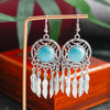 Turquoise stone earrings with silver feathers on a wooden stand